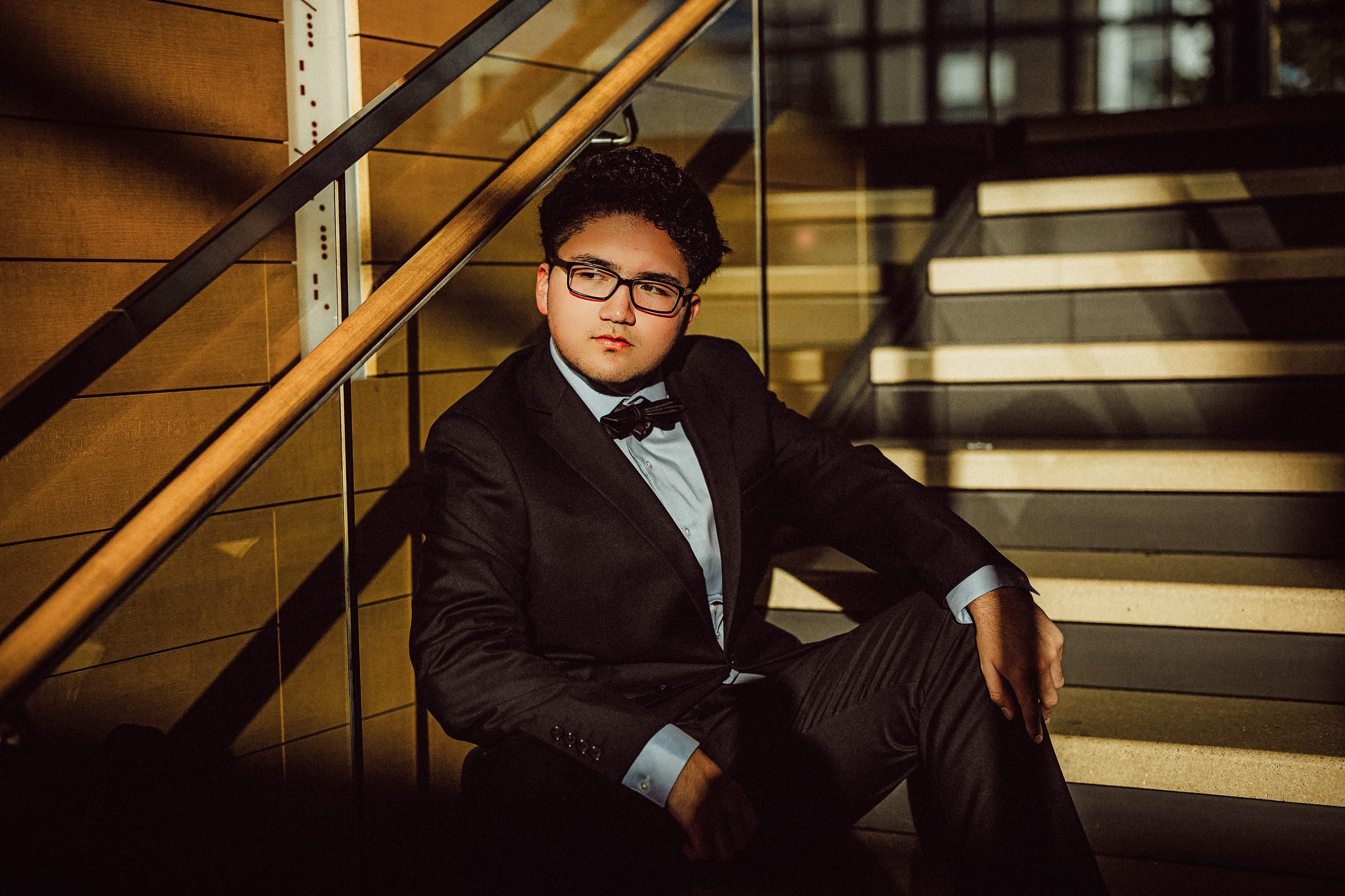 Formal portrait of a person in a dark suit seated on a modern staircase.