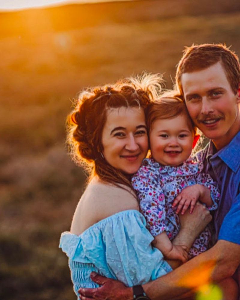 A mother, father and young daughter holding one another at golden hour