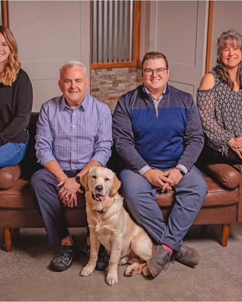 A family of four seated together indoors with their dog Clark