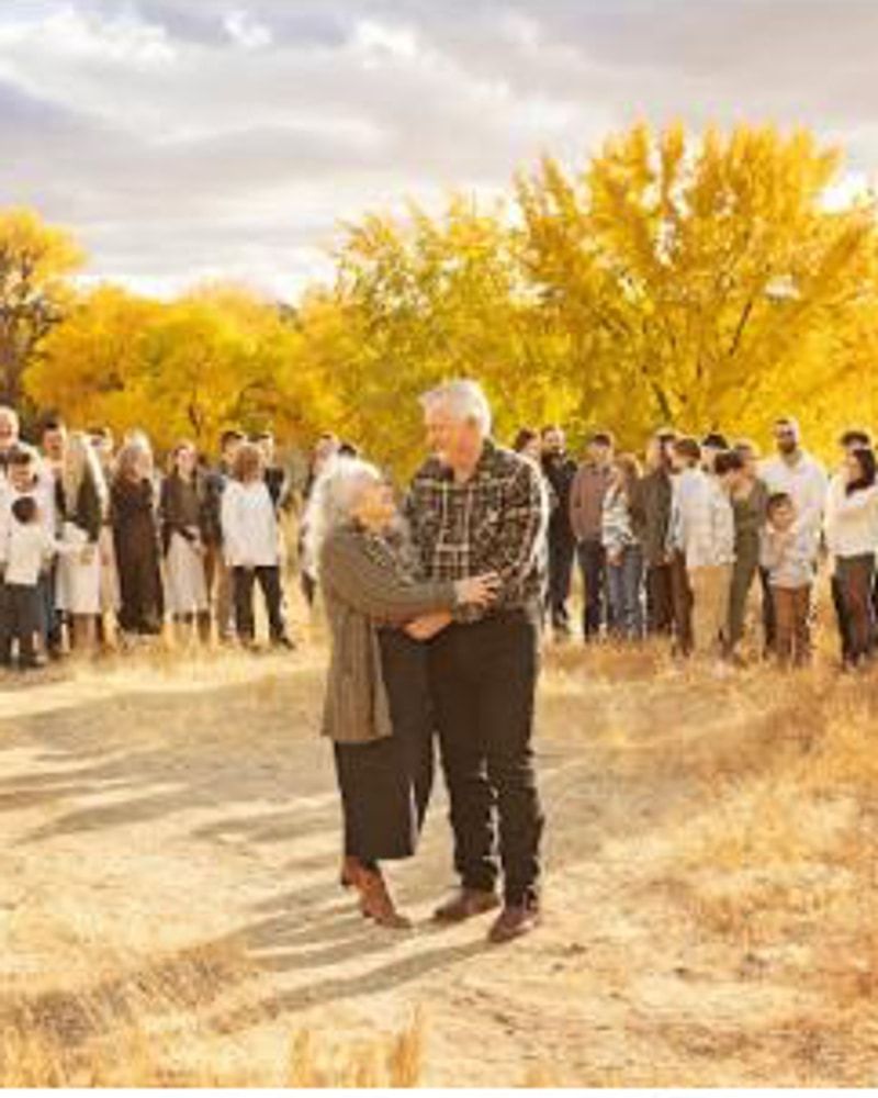 A large extended family gathered outdoors beneath golden autumn trees